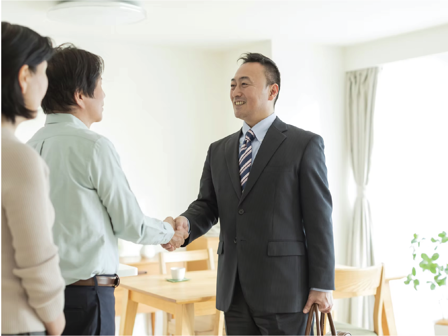 Business professional shaking hands with a couple in a home setting, symbolizing trust and relationship-building