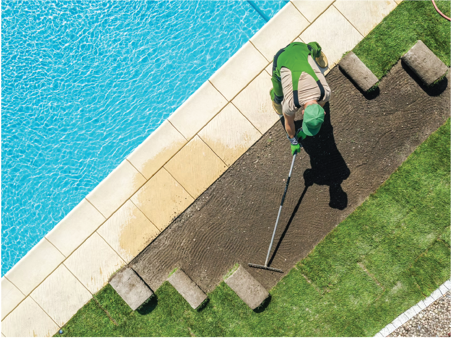 Overhead view of a landscaper laying sod beside a pool and garden edge